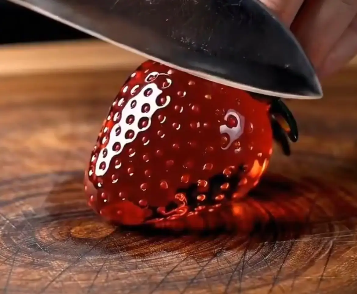 AI-generated close-up of a knife slicing a transparent red glass strawberry on a wooden cutting board