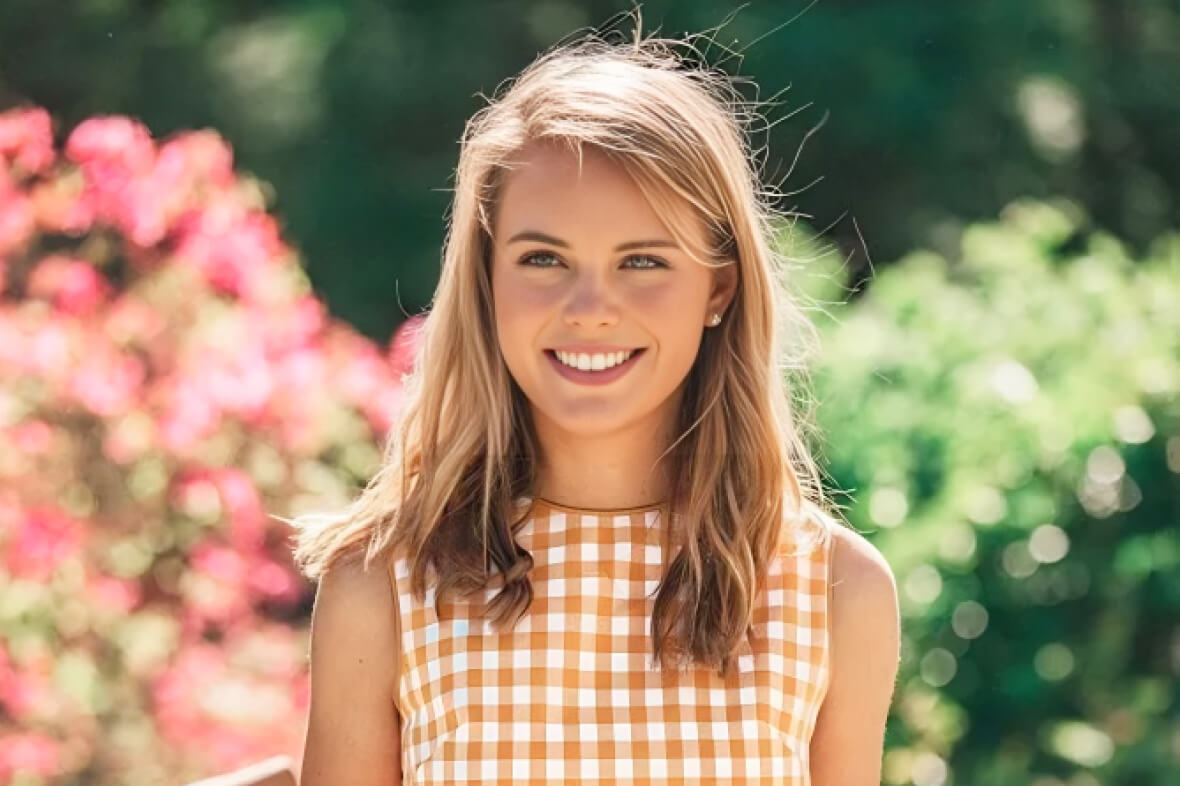 Original photo of a smiling young woman with long hair in an orange gingham top, standing in front of pink flowers and green foliage