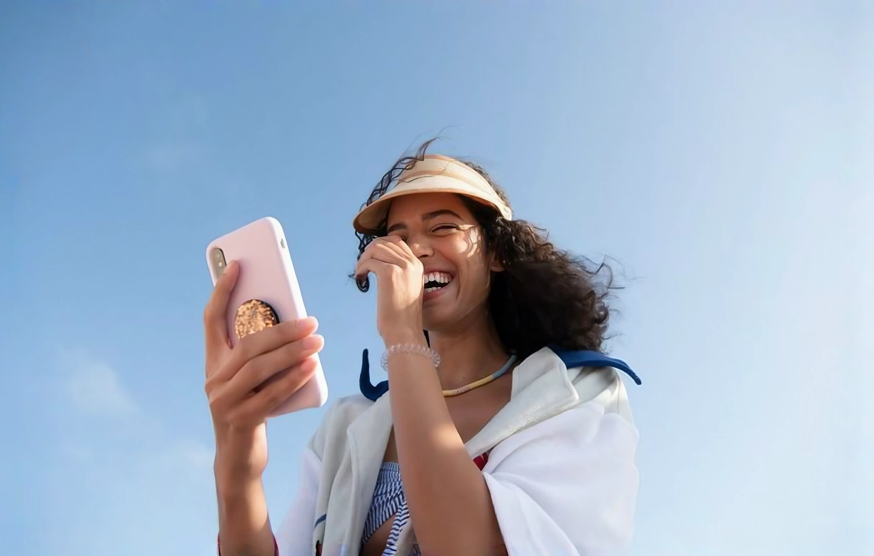 Edited photo of the same woman holding a phone, with blue sky replacing the background buildings.